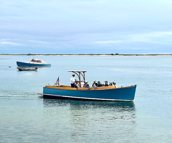A boat cruises through blue water near a sandy, grassy island under a clear sky.