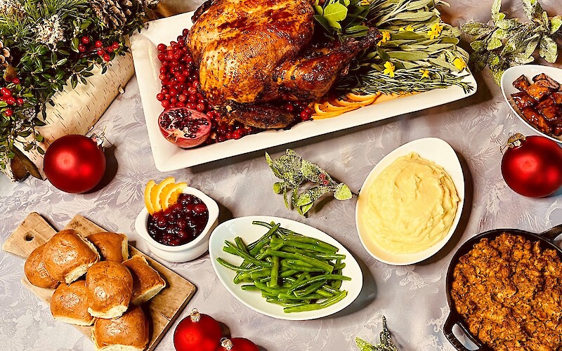 A festive meal with roast turkey, cranberry sauce, rolls, mashed potatoes, green beans, and holiday decorations completing the table.